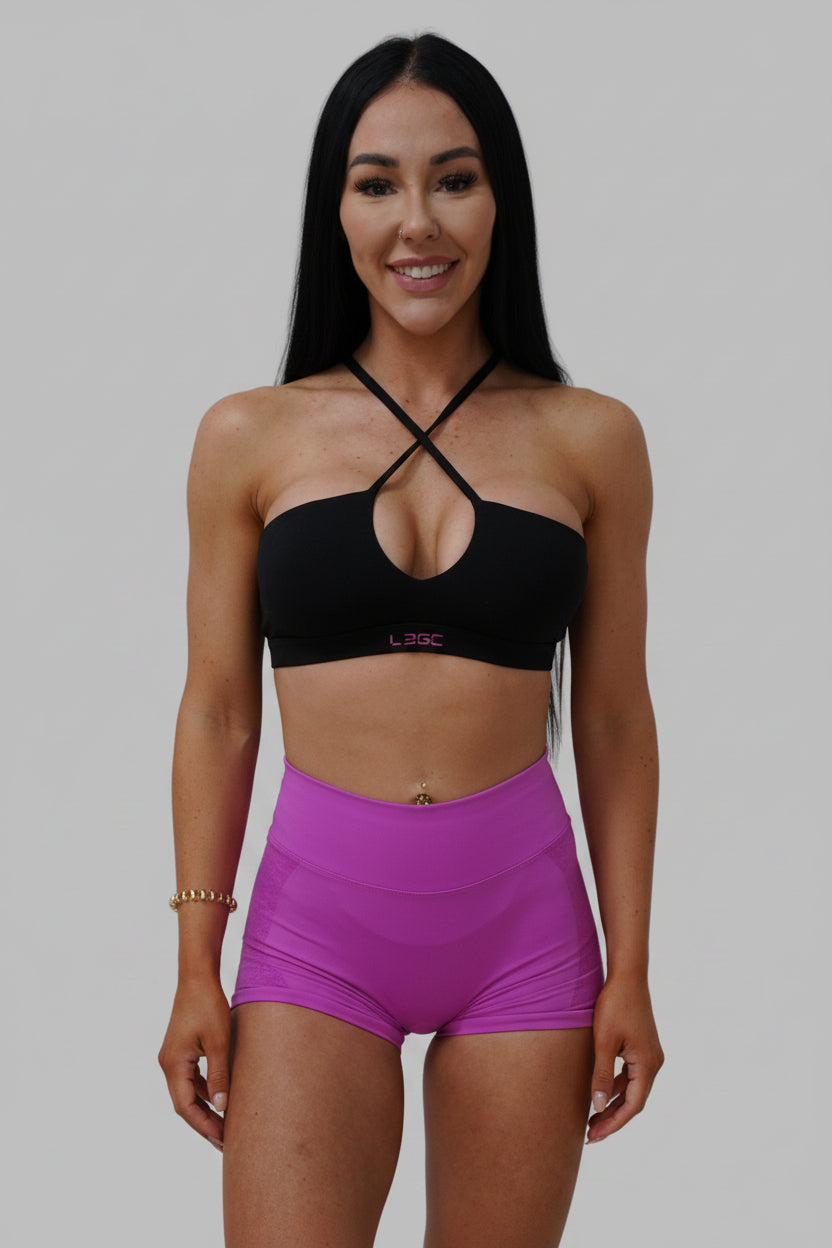 Woman in black sports bra and pink shorts.