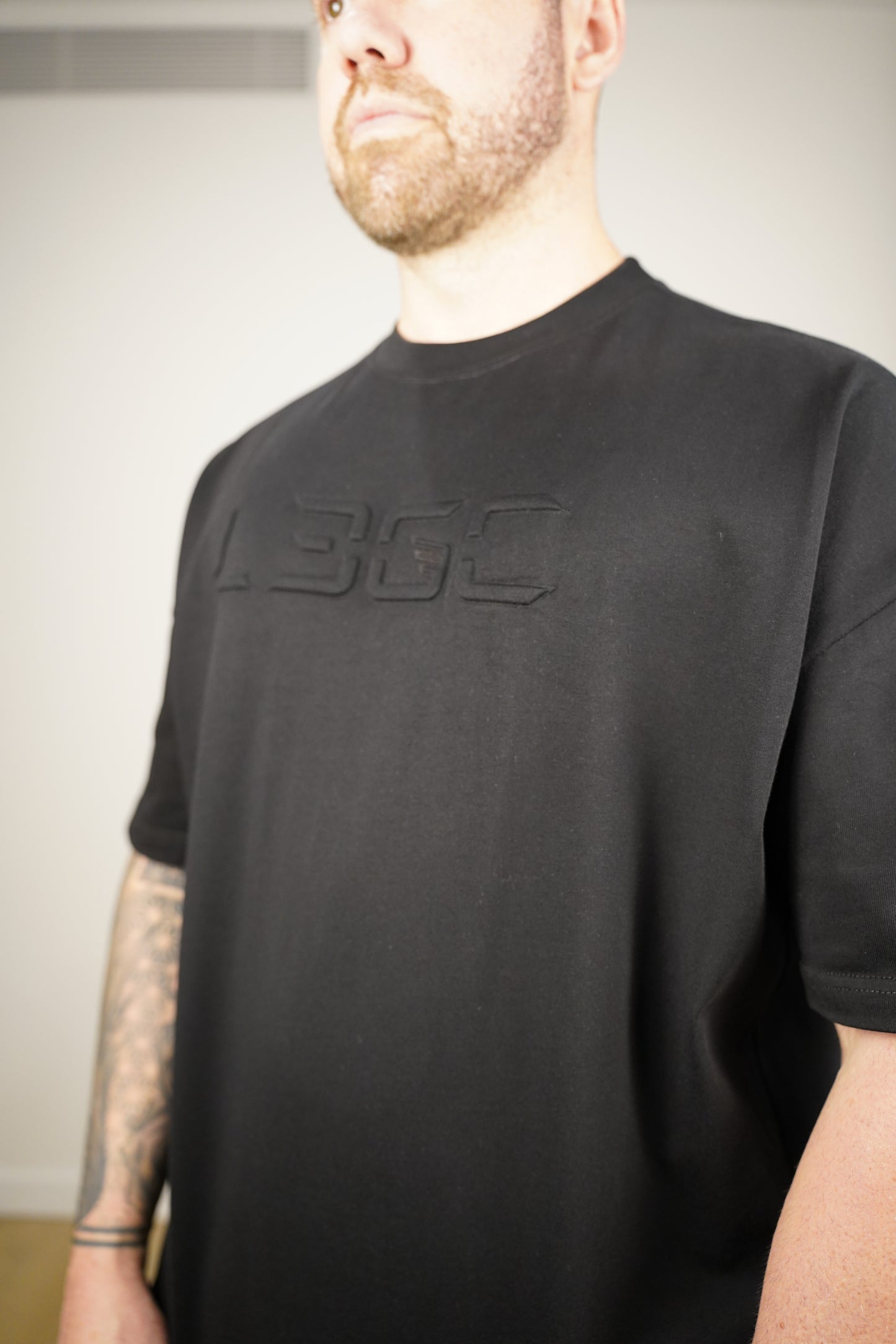 Person wearing a black t-shirt with a logo on a neutral background