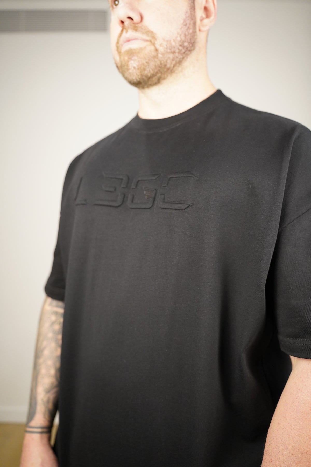 Person wearing a black t-shirt with a logo on a neutral background