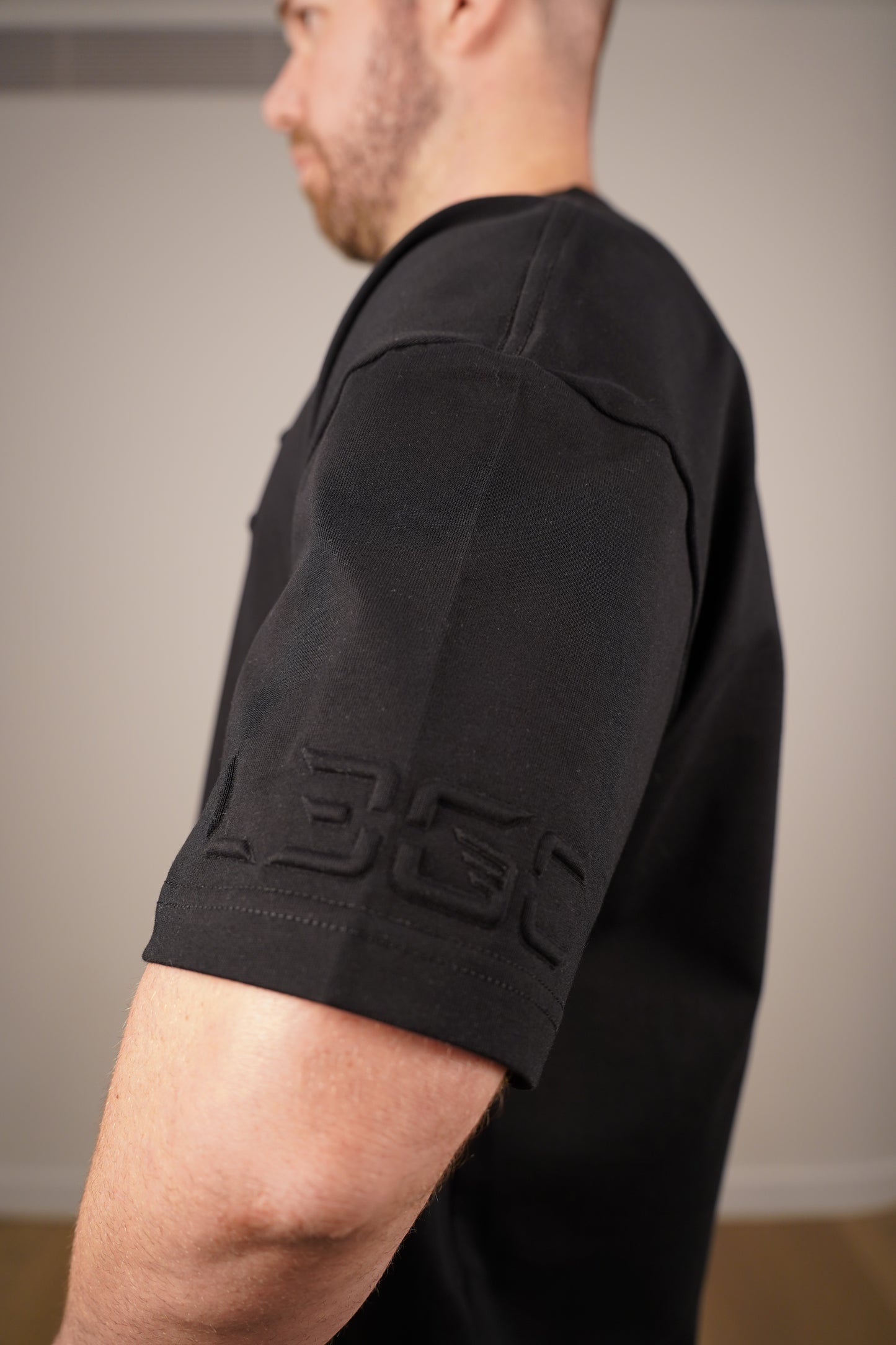 Person wearing a black tee with a brand logo on a neutral background