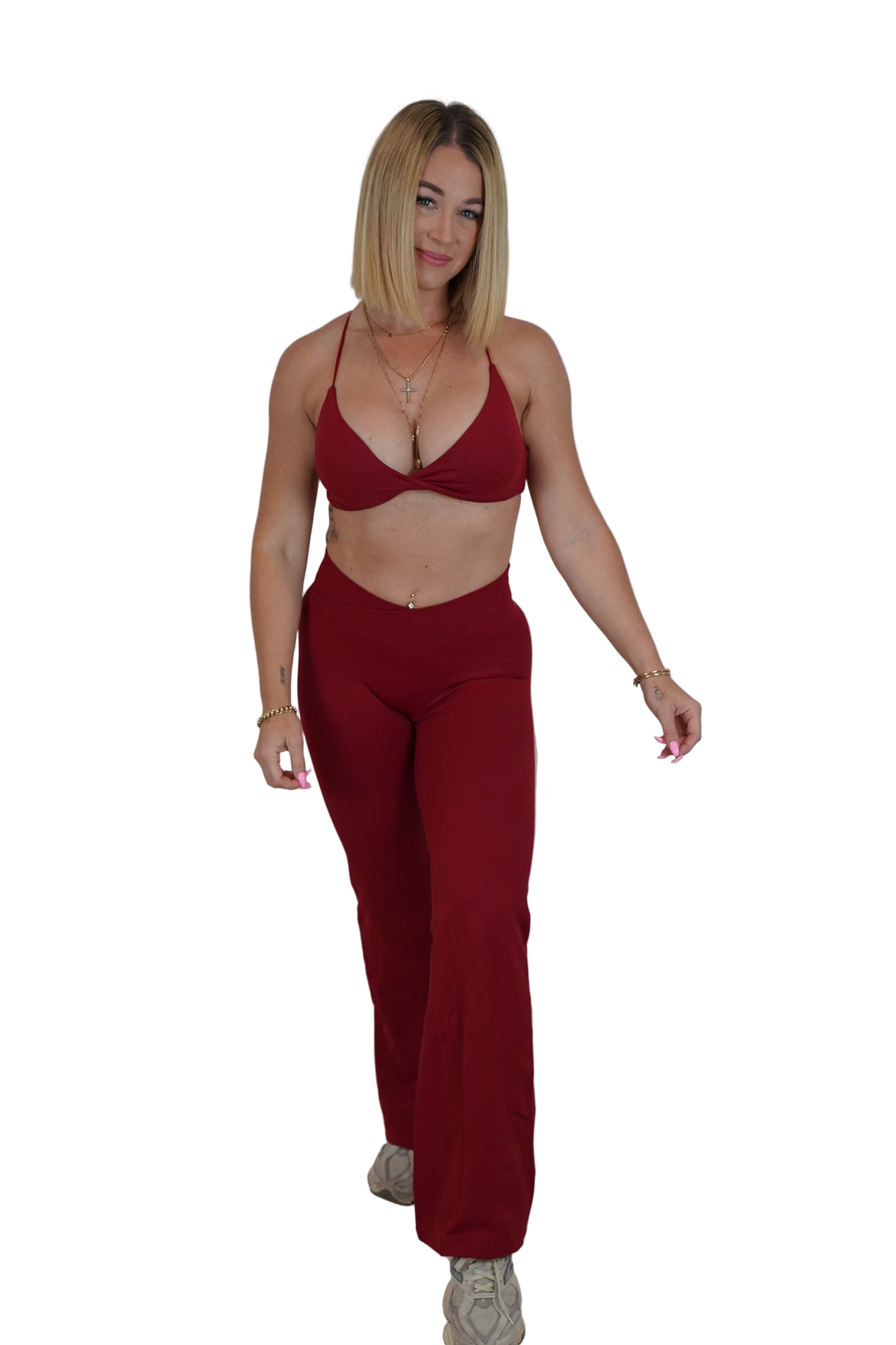 A woman modeling a matching two-piece outfit consisting of a deep red halter bralette and high-waisted wide-leg pants, standing against a white fabric backdrop.