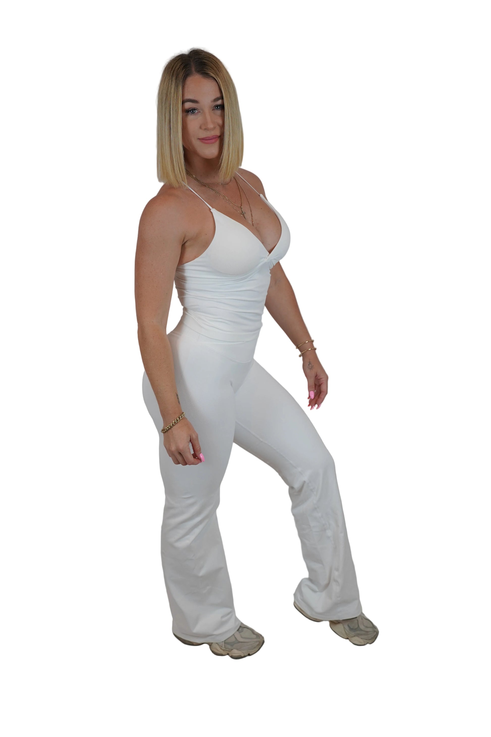 A woman modeling a white sleeveless jumpsuit with a deep V-neckline and wide-leg pants, standing against a white fabric backdrop.