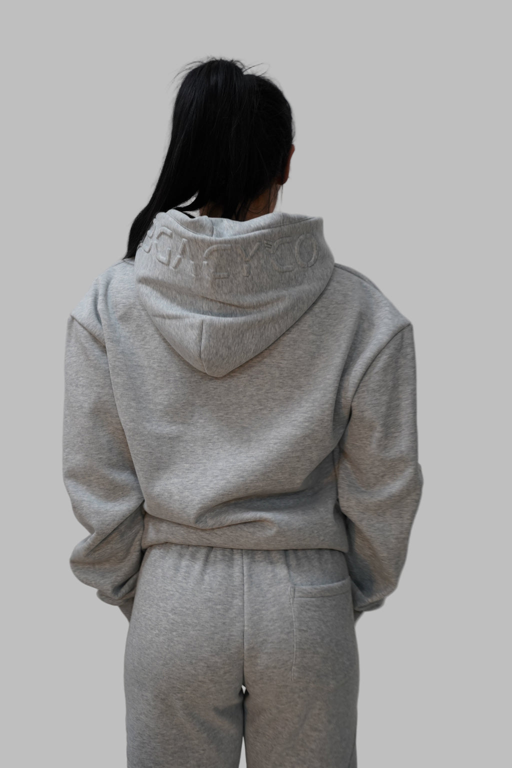 Person wearing a gray hoodie and pants on a white floor.