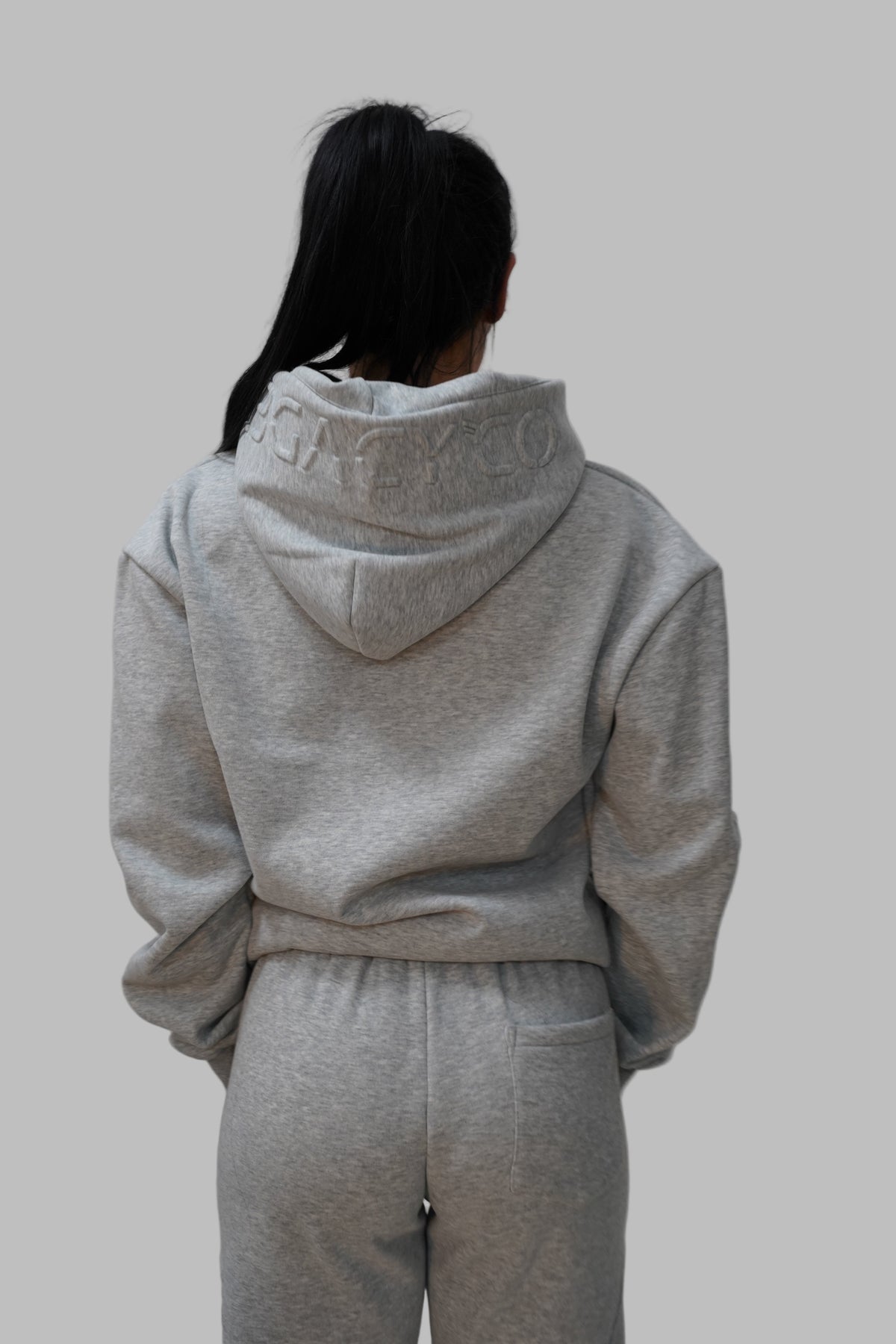 Person wearing a gray hoodie and pants on a white floor.
