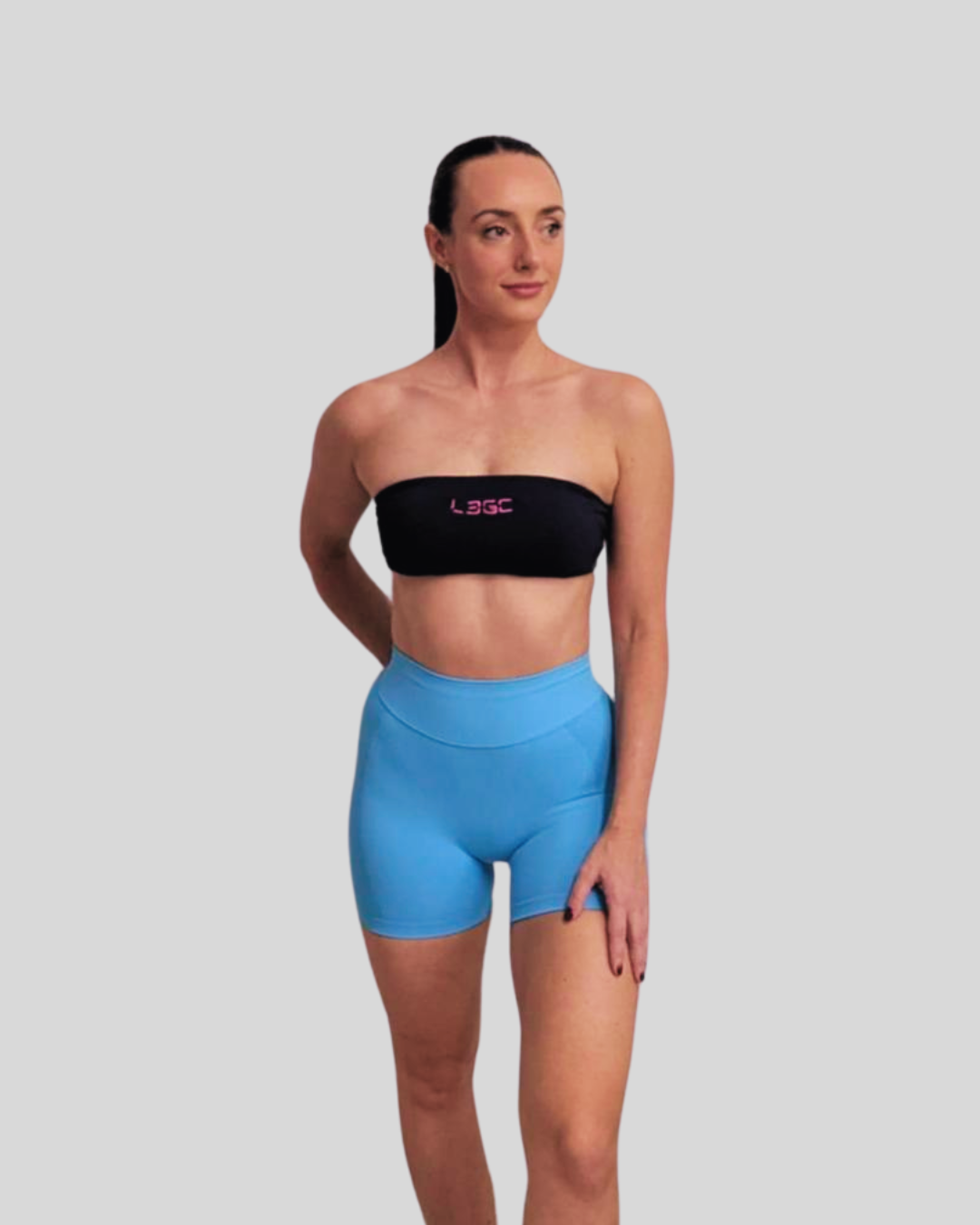 A female model wearing a blue bandeau-style sports bra with a logo on the front.