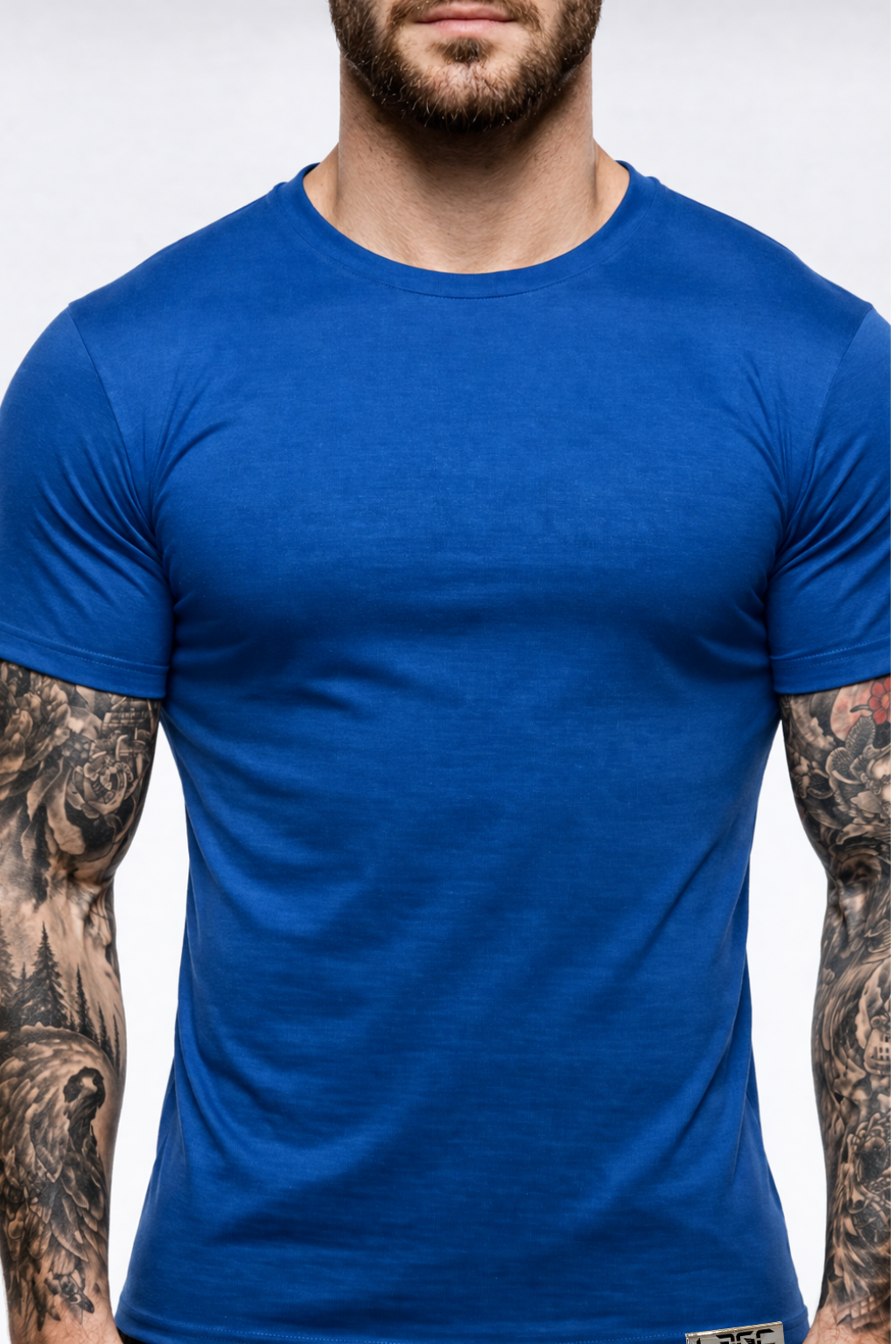 Man wearing a blue t-shirt with tattoos on arms against a white background
