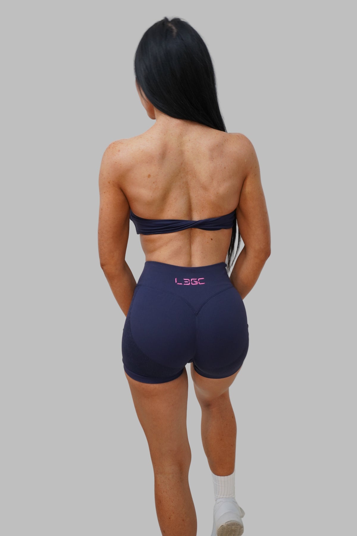 woman wearing a navy blue sports bra and shorts with legc branding standing against a white wall.