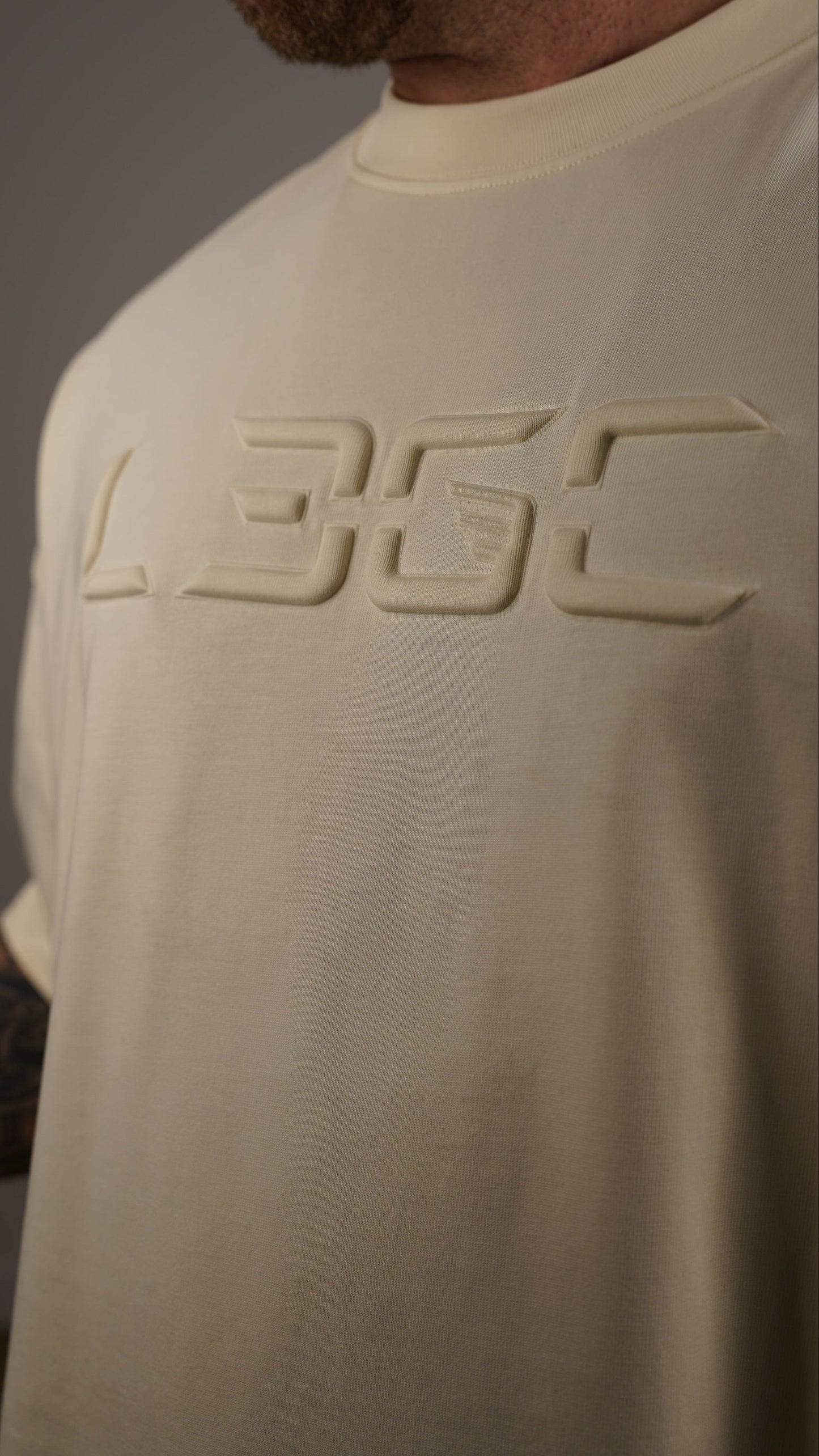 Person wearing a beige shirt with a logo on the back against a neutral background