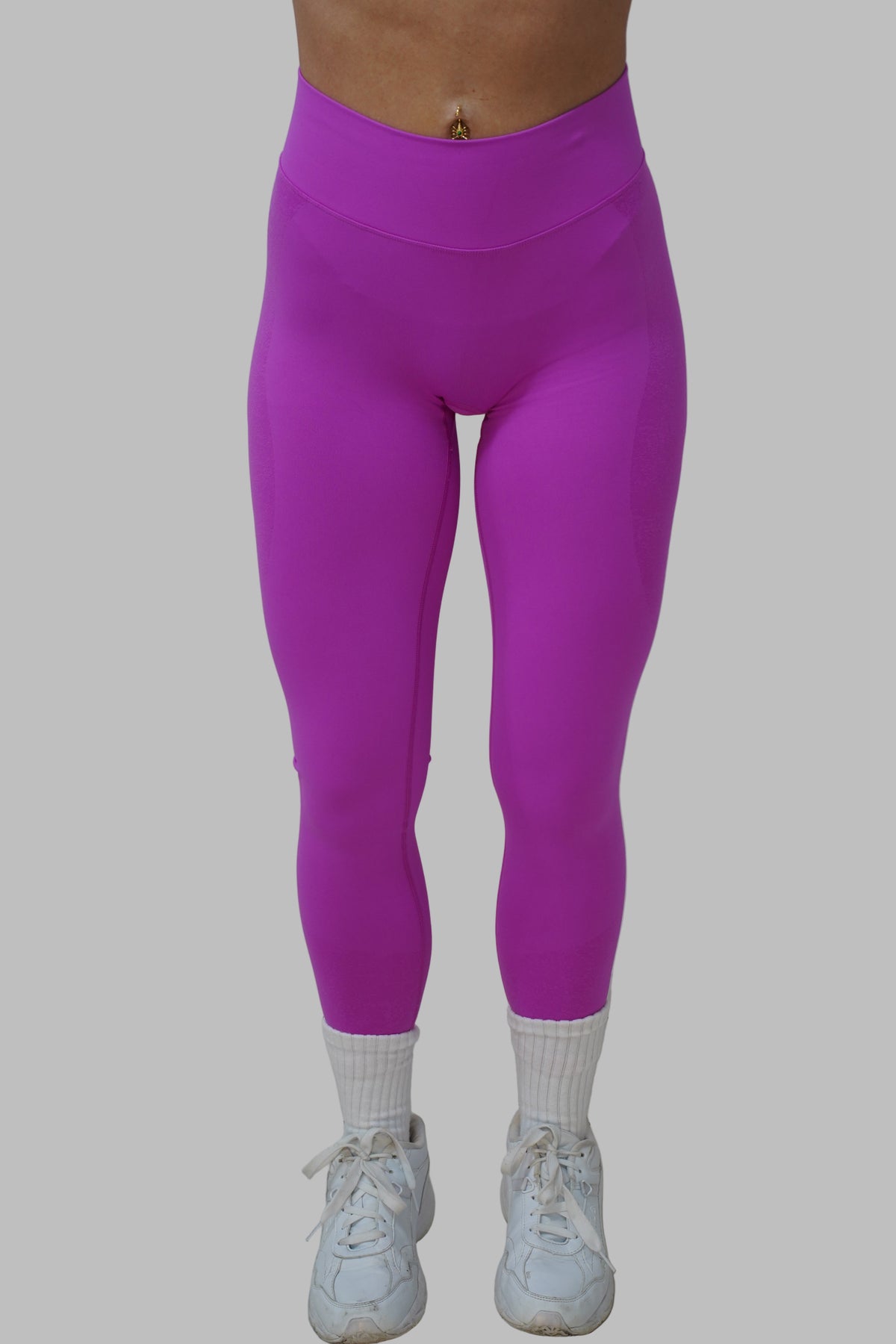 woman wearing pink leggings and white sneakers on a neutral background