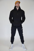 Man wearing a black hoodie, black pants, and white sneakers standing in front of a metallic shutter.