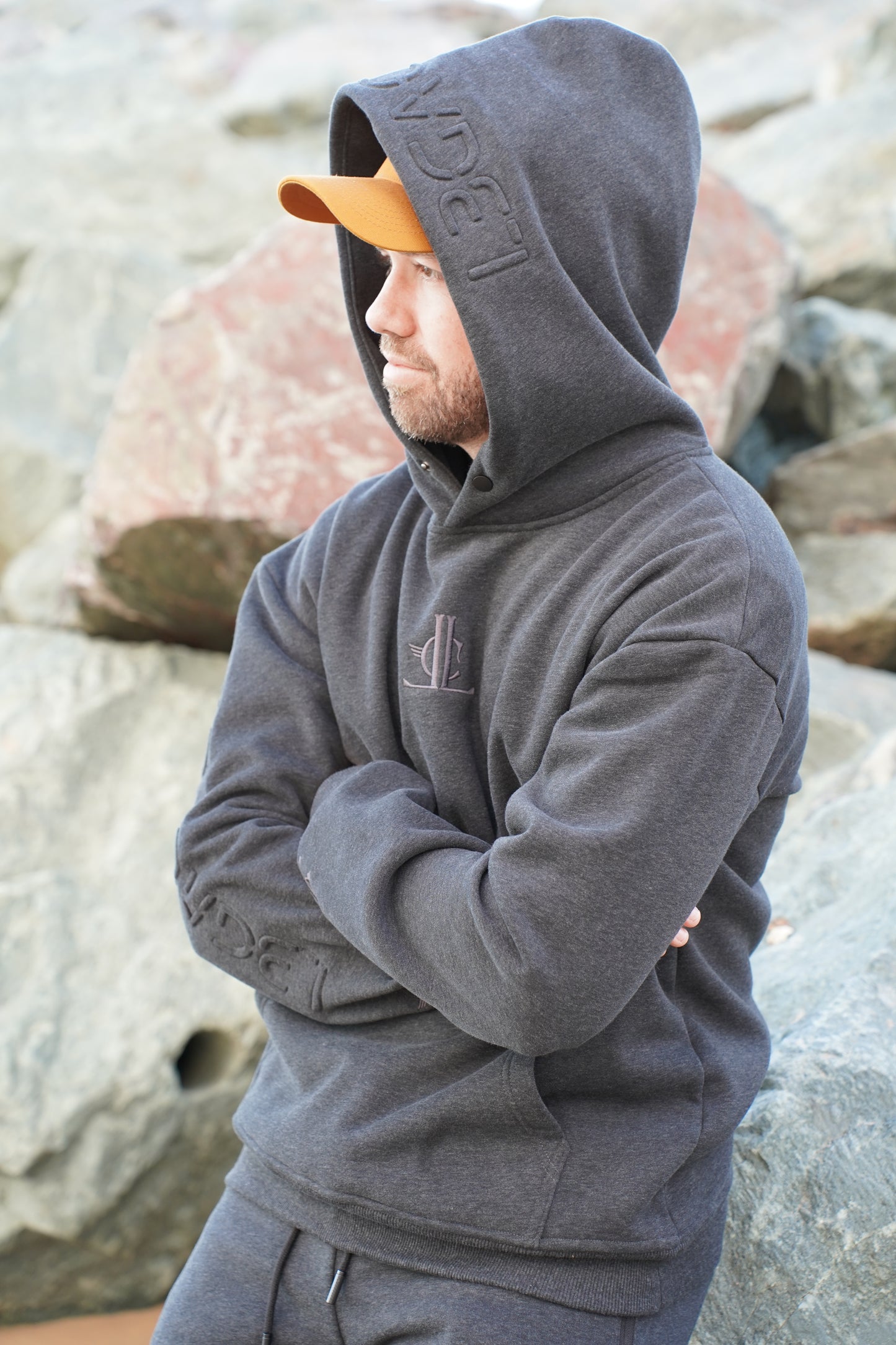 Person wearing a gray hoodie with a brand logo, standing against a rocky background