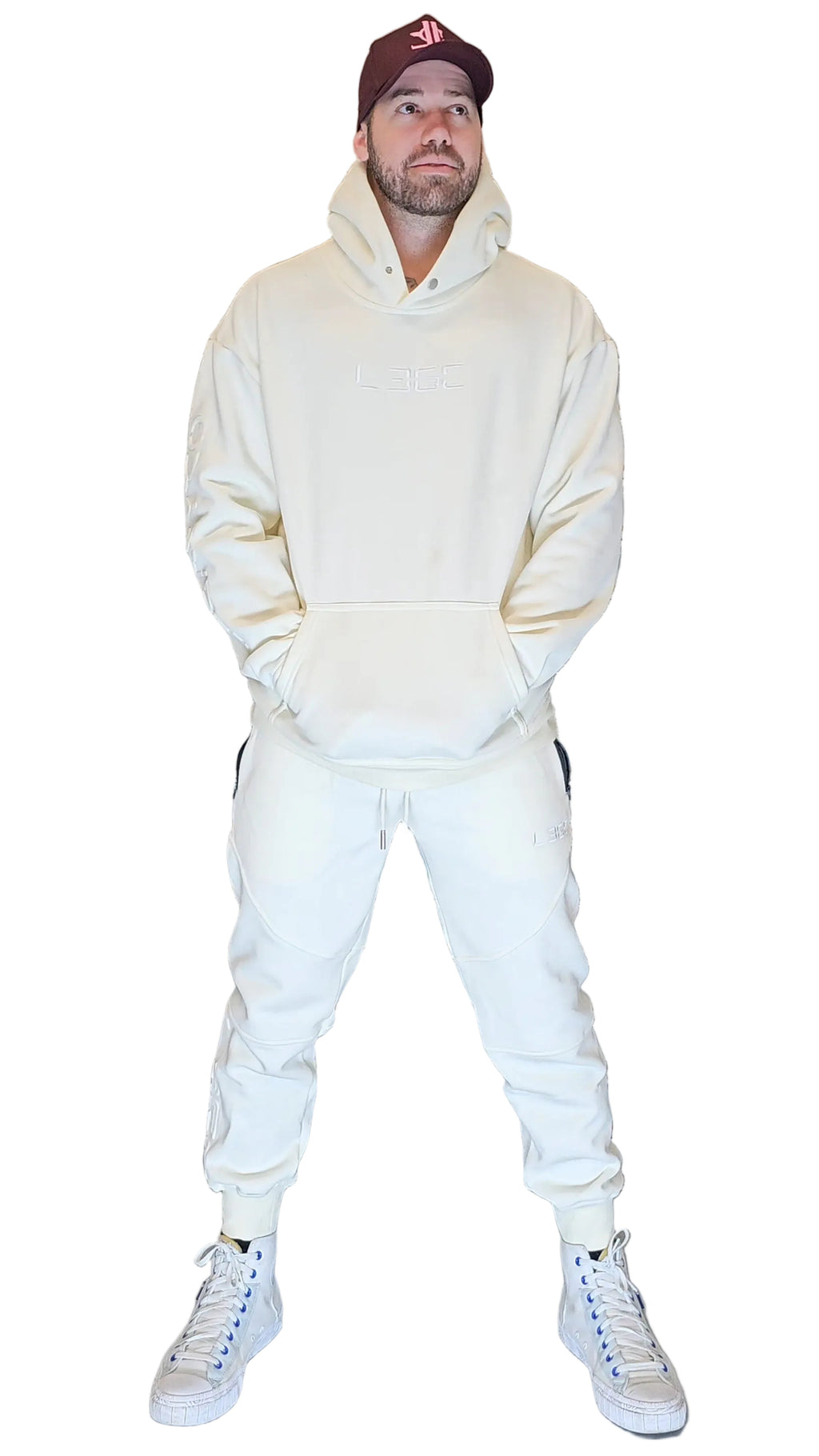 Person wearing a cream hoodie and pants with white sneakers against a metallic shutter background
