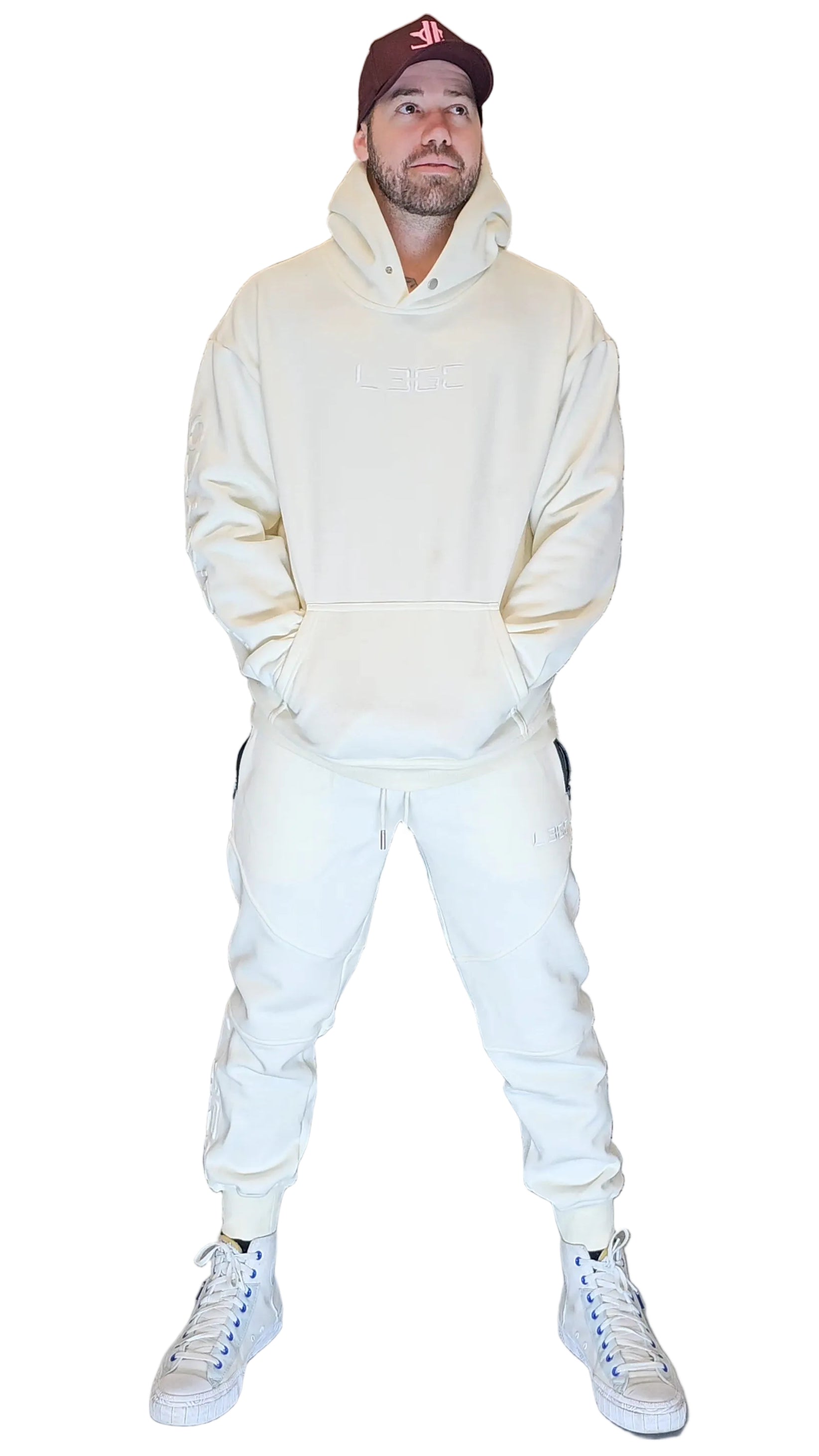 Person wearing a cream hoodie and pants with white sneakers against a metallic shutter background
