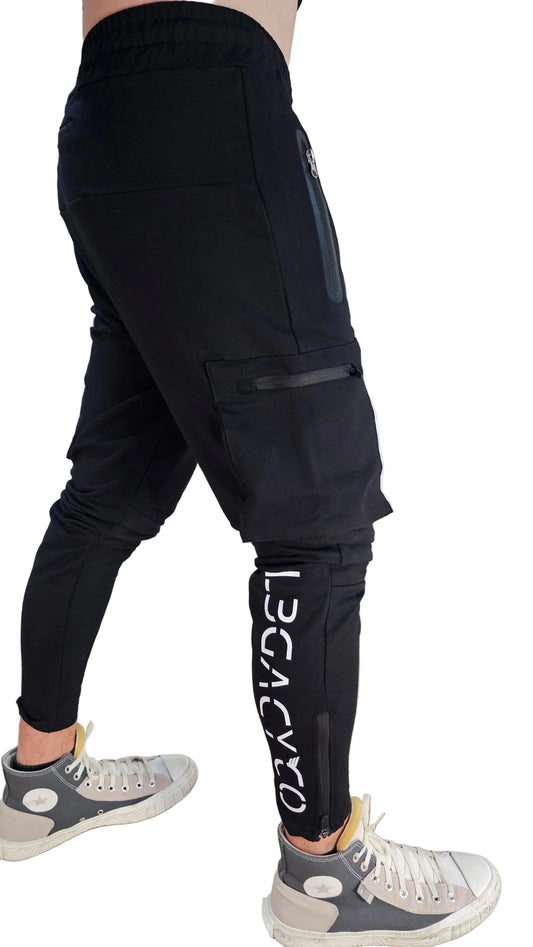 A person wearing black Raptor joggers with a visible brand logo on the leg, standing in a room with shelves in the background.