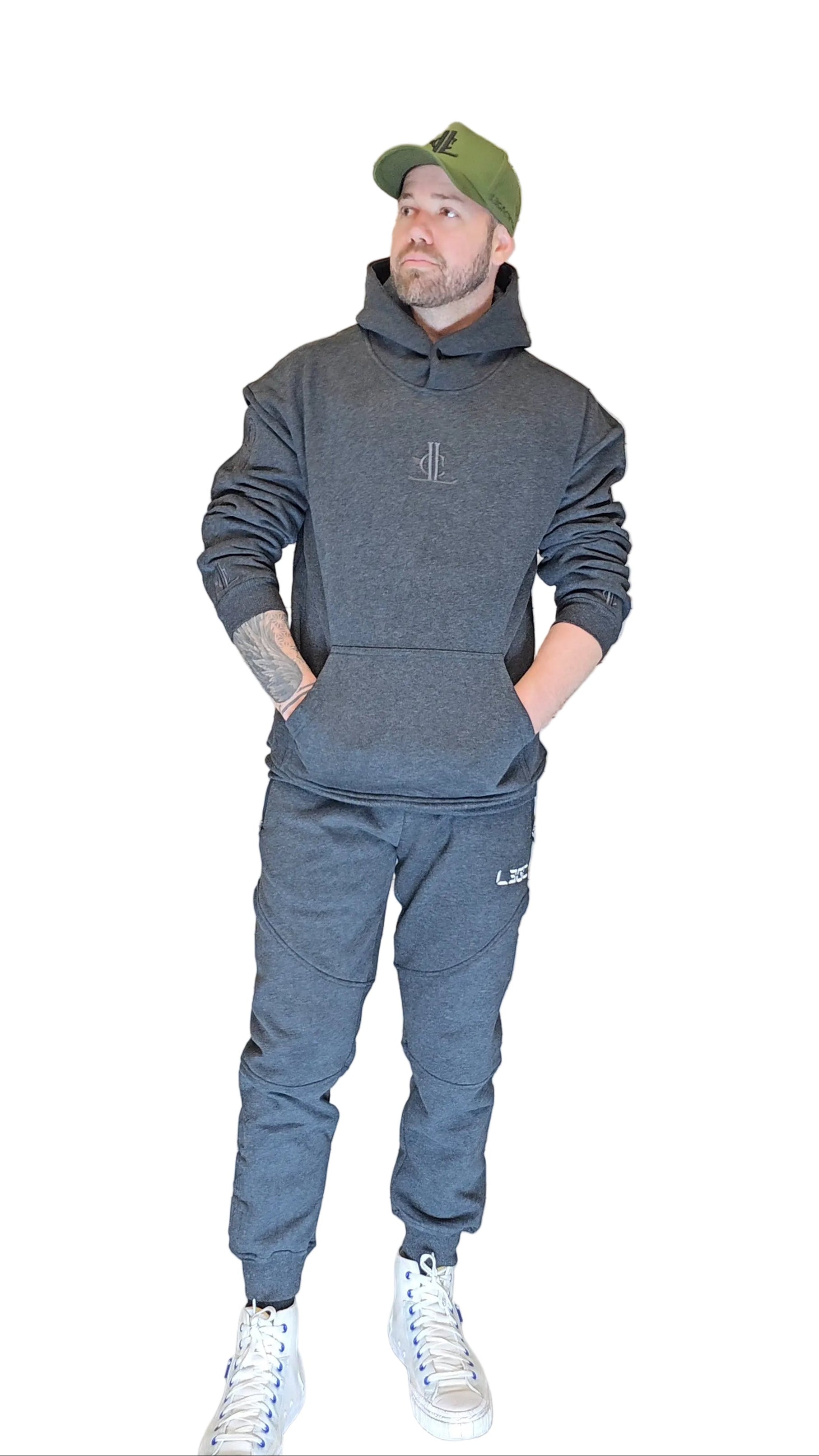 Person wearing a gray hoodie and pants with a green cap, standing in front of a metallic shutter.