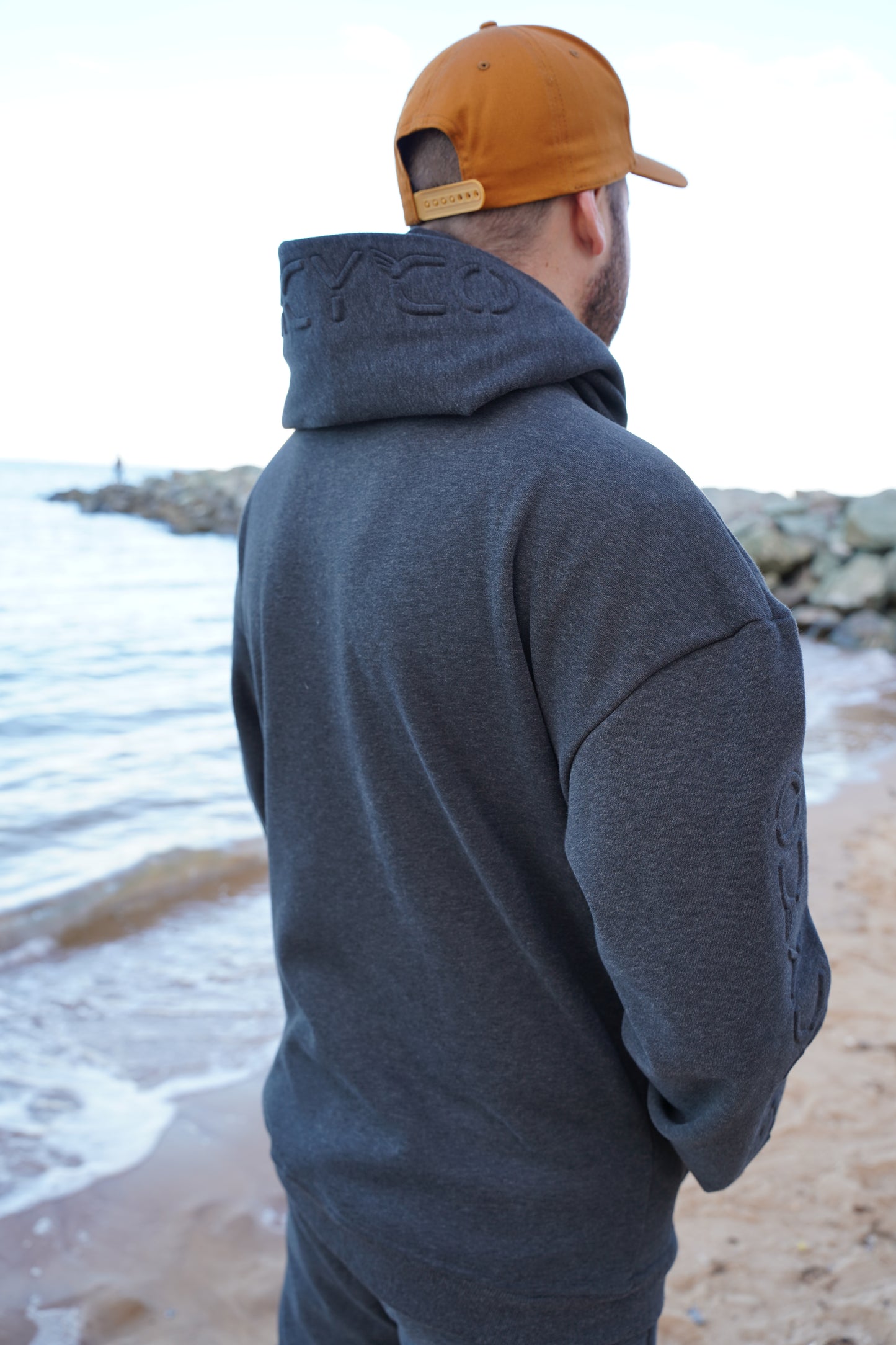 Person wearing a gray hoodie and brown cap against a light-colored wall.
