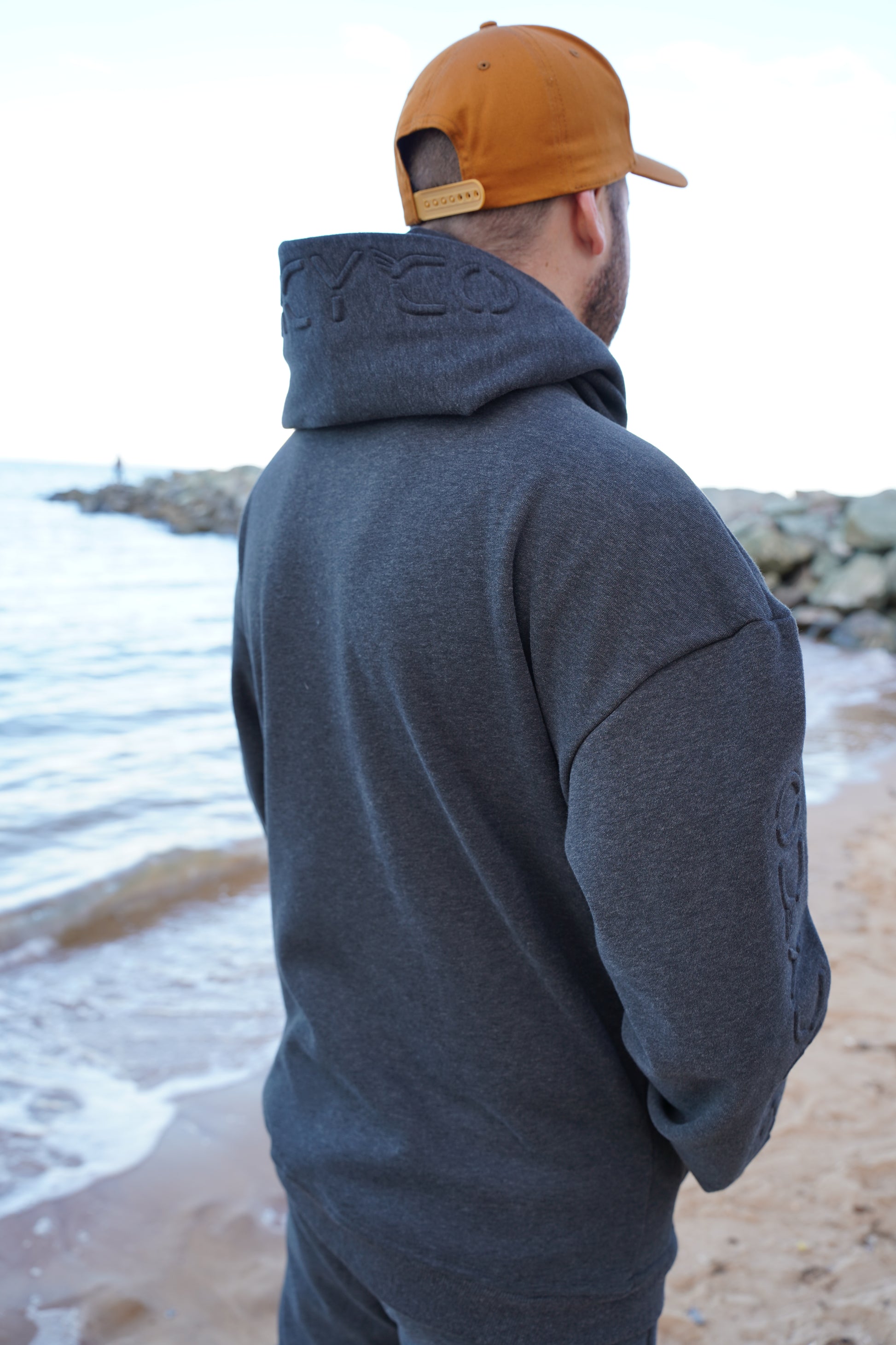 Person wearing a gray hoodie and brown cap against a light-colored wall.
