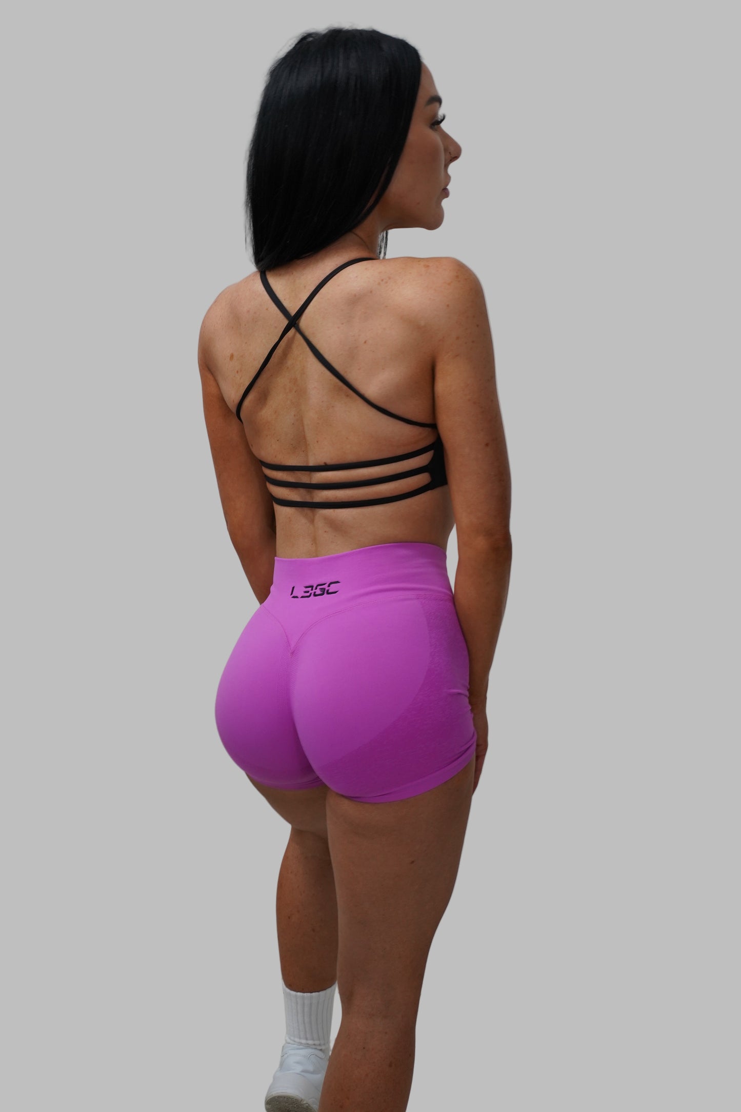 Woman wearing a black sports bra and pink shorts with a black brand logo.